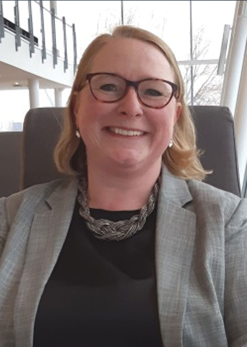 Professionelles Porträt einer lächelnden Frau in grauem Blazer.