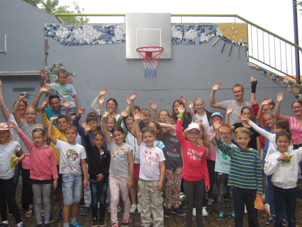 Große Gruppe von Kindern und Jugendlichen winkt im Freien.
