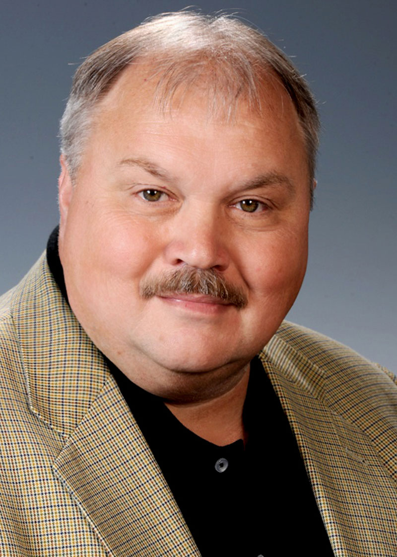 Porträt eines Mannes mit Schnurrbart in kariertem Sakko.