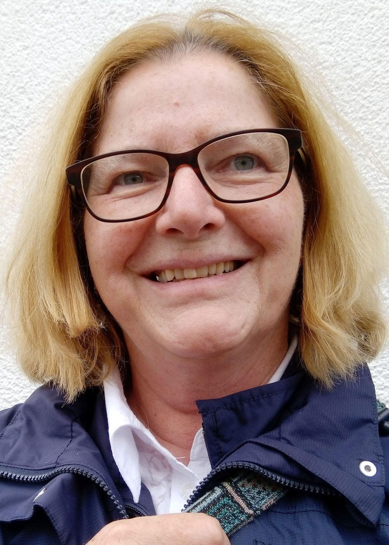 Porträt einer lächelnden Frau mit blonden Haaren und Brille.