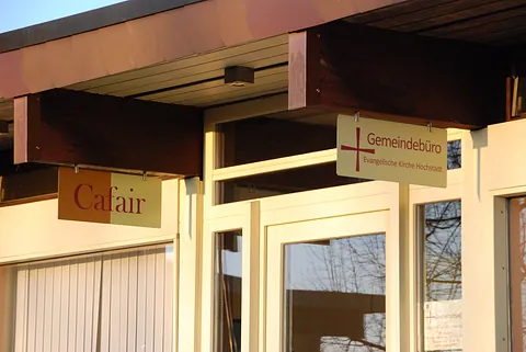 Schilder für "Cafair" und "Gemeindebüro" am Kirchengebäude.